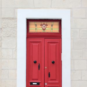 Nancy stained glass window film in an orange, yellow and red colour and a center house number installed above a red door.