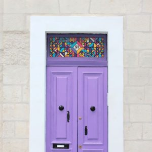 A colourful stained glass window film with a central door number installed above a purple door