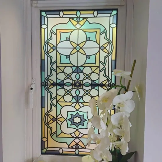 Zak stained glass window film with Victorian detailing in pastel colours installed on a window with matching plants in front.