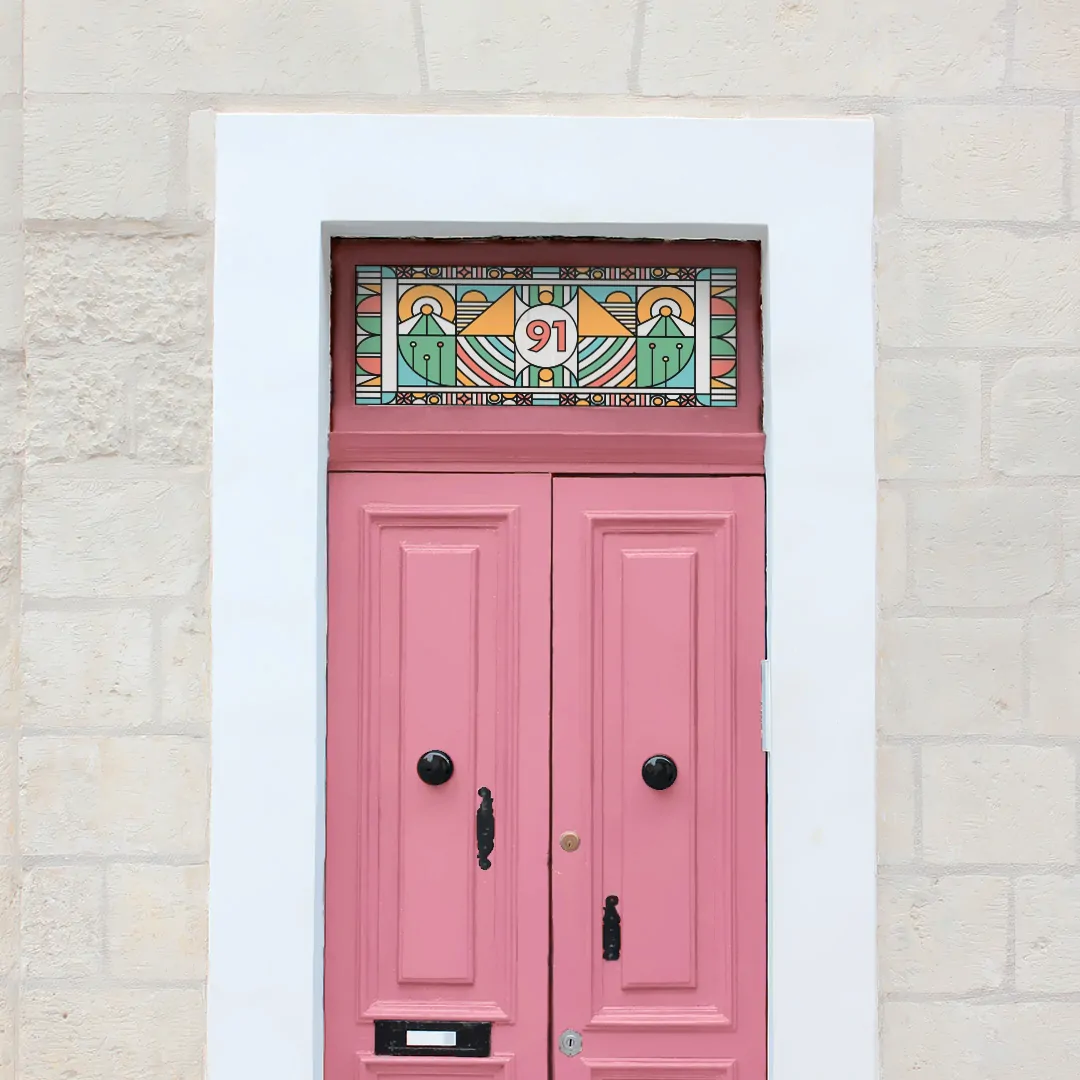 A colourful and intricate stained glass window film with a central door number installed above a pink door