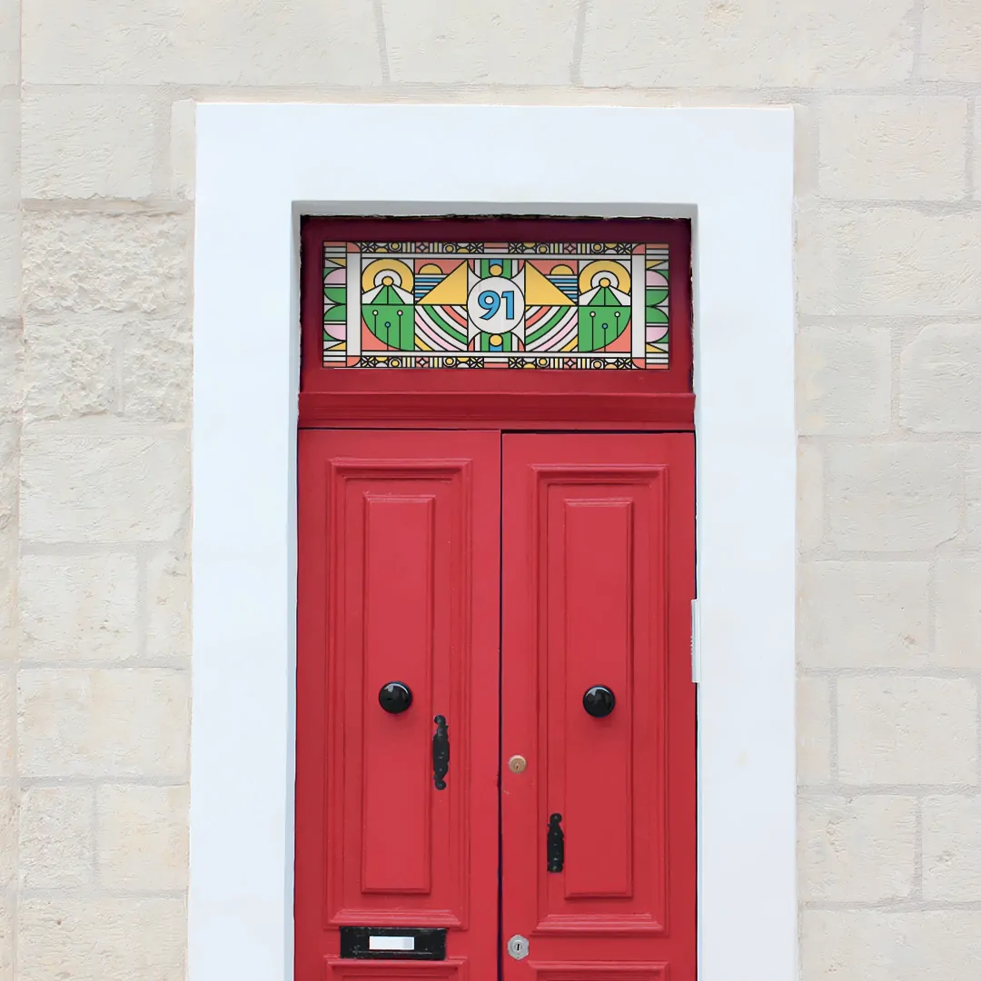 a bright and colourful modern stained glass window film with a central door number installed above a red door